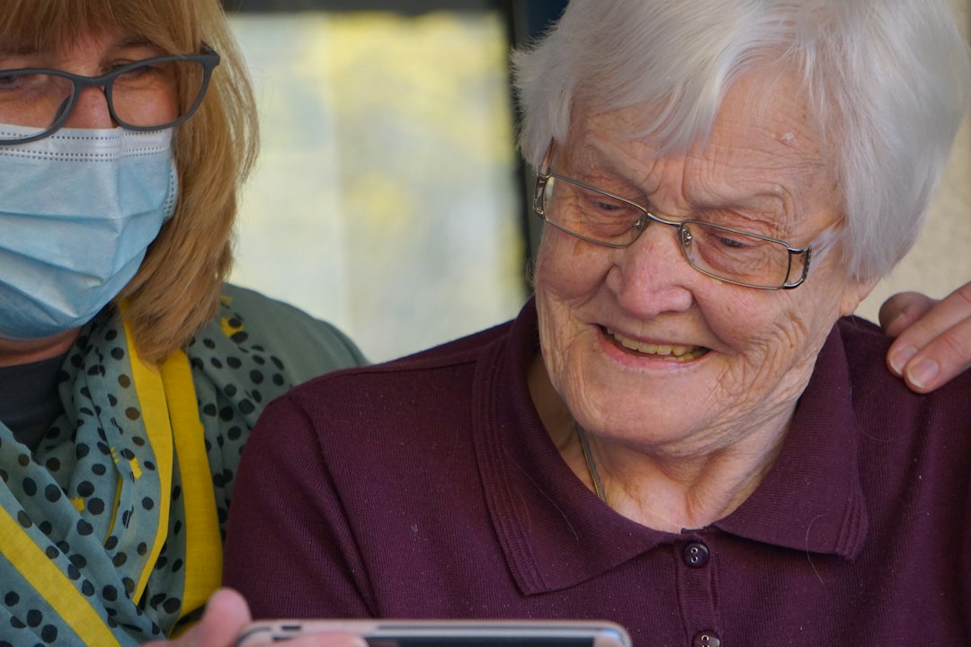 Caregiver helping a smiling elderly woman use a health monitoring app on a smartphone