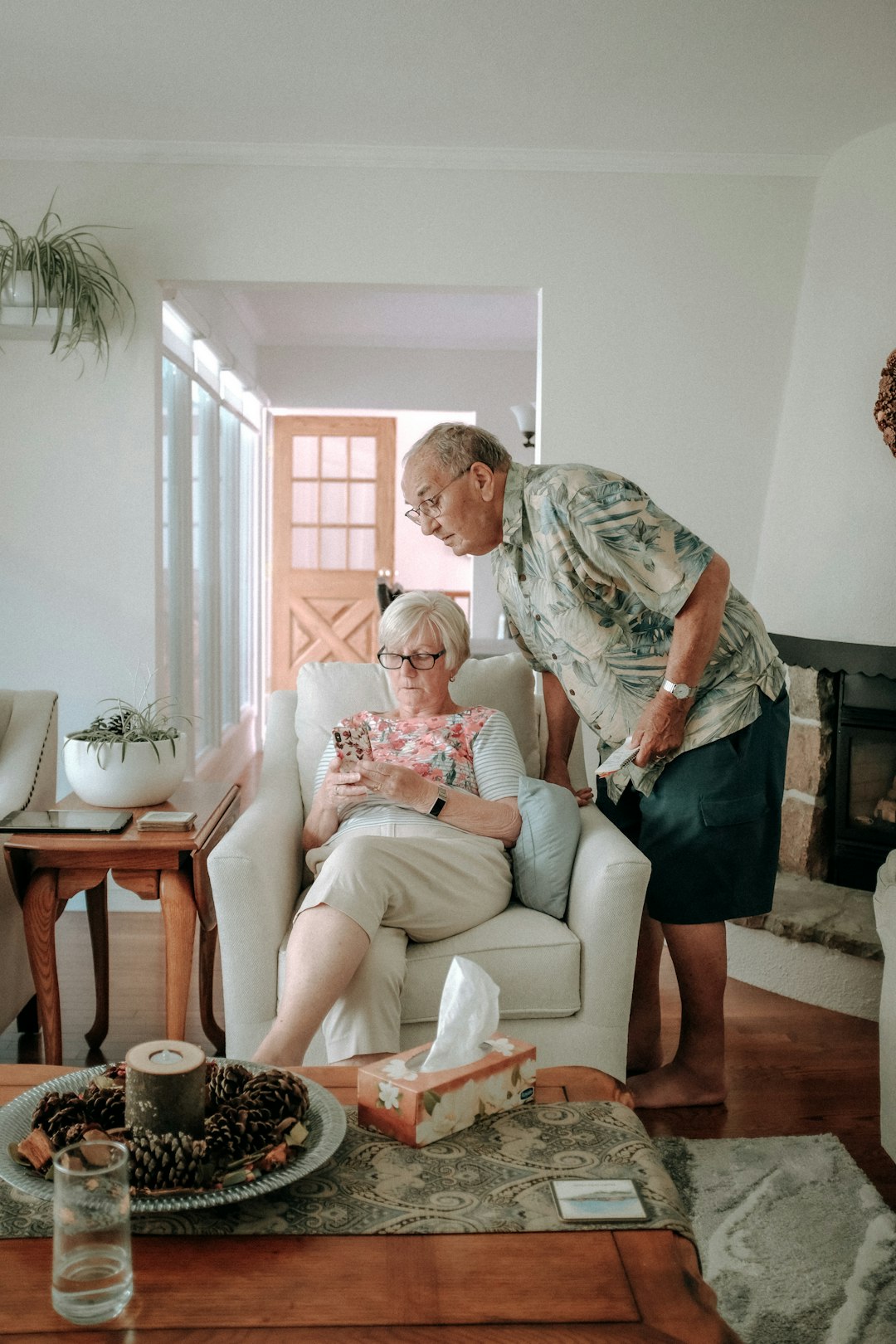 Elderly woman relaxing in an armchair at home while family member stands nearby, aging in place